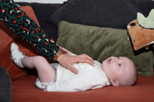 b&eacute;b&eacute; sur un canap&eacute; avec la main de sa m&egrave;re qui le chatouille