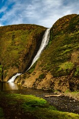 some water that is near a large waterfall with green grass