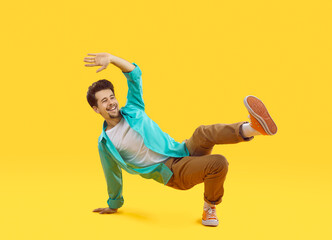 Positive cheerful young casual man funny doing breakdance dance moves isolated on orange...