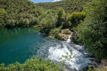 Naklejka na ściany i meble Tranquil scene of a lake surrounded by greenery near the Kravica Waterfall in Bosnia and Herzegovina
