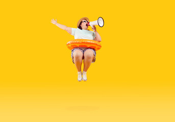 Full body photo of a happy funny fat plus size overweight woman in sunglasses with rubber ring jumping and speak in mouthpiece on studio yellow background. Summer holiday trip and vacation concept.
