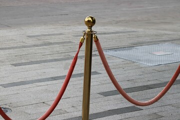 A sidewalk red velvet rope attached to a gold plated standard for lines forming for patio seating.