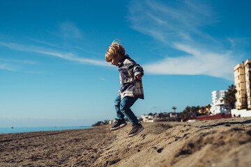 The boy jumps up on the sandy beach near the sea. a 3-year-old boy in a checkered shirt plays on the sand. cheerful active baby jumping on the sand