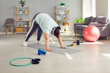 Fat, chubby, overweight, plus size, young woman doing fitness exercises on a rubber sports mat during her weight loss fitness workout in the living room at home