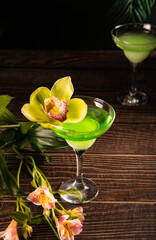 Cold green exotic cocktail with decorated flowers orchid and palm leaves. Tropical vibes.