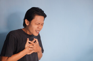 Asian young man in black t-shirt with chest pain expression