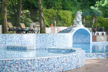 View of the hotel with swimming pool with mosaic tiles, sun loungers, a statue, a lion figure...