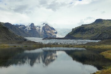 Fototapeta na wymiar Tranquil lake in a lush meadow surrounded by snow-capped mountains and a glacier in the distance