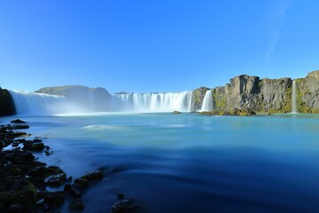 Tranquil Godafoss waterfall cascading down a rocky cliff on a sunny day in Iceland