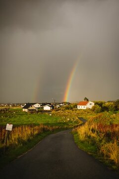 Double vibrant rainbow arching over a village with a small stream in the foreground