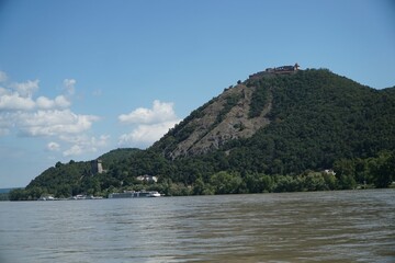 Fototapeta na wymiar Majestic mountain surrounded by lush trees along the banks of a tranquil river in Visegrad, Hungary