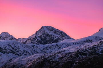 Scenic view of majestic snow-capped mountain peaks illuminated by a beautiful pink-hued sunset.