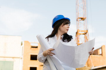 Plus size woman engineer in a white shirt and blue helmet is holding blueprints. Female in blue...