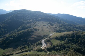 Obraz premium Scenic landscape of a green mountainous terrain featuring lush green trees, against the bright sky