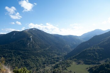 Scenic landscape of a green mountainous terrain featuring lush green trees, against the bright sky