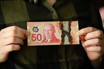 A bill of fifty Canadian dollars in the hands of a girl. The concept of earnings, savings