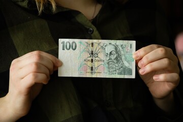A bill of one hundred Czech crowns in the hands of a girl. The concept of earnings, savings