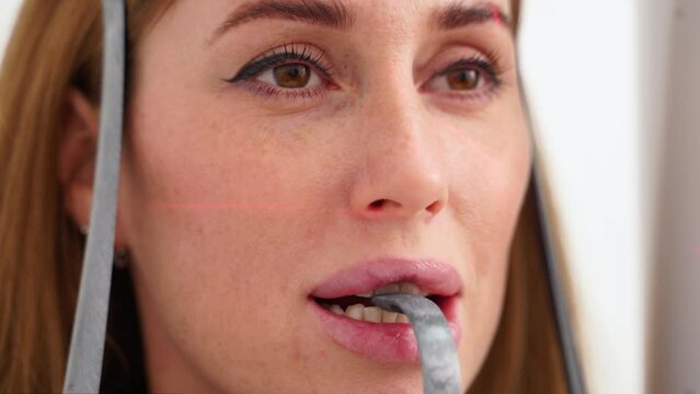 Close-up of woman's face with head positioned in cephalometric panorama x-ray machine. Female patient stands in dental x-ray machine for dental radiography. Woman making panoramic shot of the jaw.