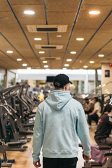Anonymous Athlete Walking Among Gym Machines Whit a Cap On. Unrecognizable young athlete walking among gym machines, cap on.