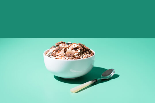Cereal de granola muesli en un tazón blanco con cuchara sobre fondo verde	