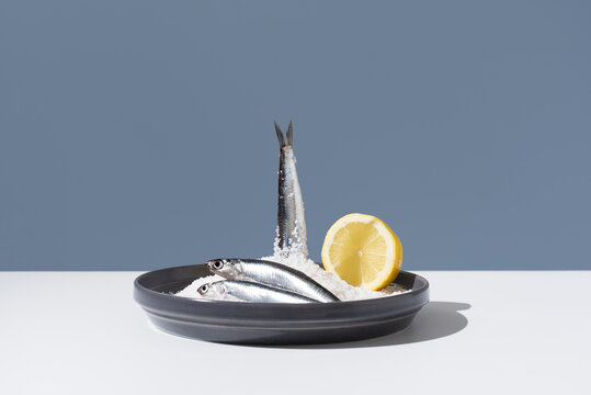 Tres anchoas frescas con medio limón sobre un plato lleno de sal sobre fondo azul	
