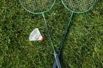 leisure games and sport equipment concept - close up of badminton rackets and shuttlecock on grass