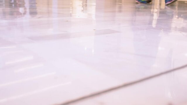 reflection on the floor of the legs of anonymous people walking through a shopping mall. They are shopping carefree to feel fashionable in a capitalist world of consumption