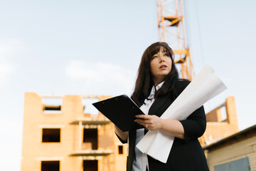 Plus size woman engineer in a white shirt and black jacket is holding blueprints. Plus size female...