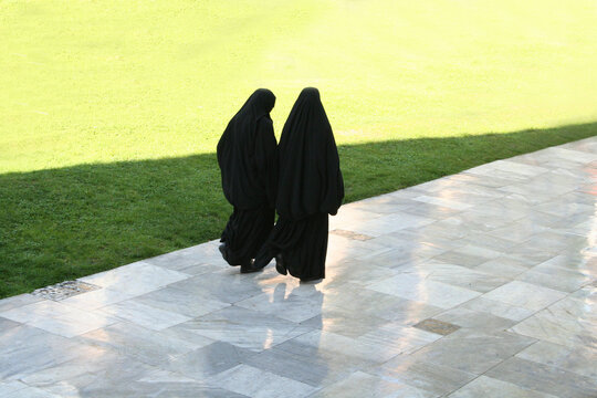 Two Arab women strolling in a garden on a sunny day..