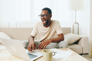 Smiling African American Freelancer Typing on Laptop at Home Modern Technology and Cyberspace in Millennial Lifestyle This image depicts a young and happy African American man working on his laptop,