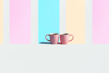 Minimalistic image of two pink coffee cups on a surface with pastel blue, peach powder, white and pink vertical striped background. Minimal concept of coffee culture. Copy space,