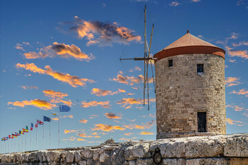 Medieval Mandraki harbor with windmills and international flags in medieval city of Rhodes, Greece