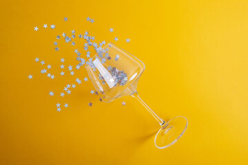 Confetti in the shape of stars is poured into glasses of champagne on a colored background. Festive mood place for text