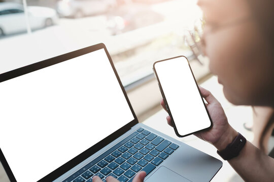 Close-up image of a woman sitting in the cafe and using her smartphone and laptop. smartphone and laptop white blank screen mockup for display your graphic banner.