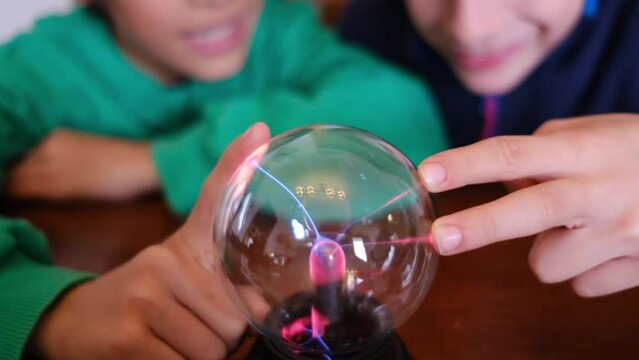 Young boys mesmerized by a plasma ball's lightning during a study session at the table