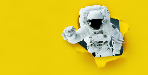 Space man astronaut tears paper from hole, concept. Yellow banner for design and text. Creative...