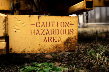 Caution! Hazardous Area. A red painted stencil on old rusty yellow metal. The steel of an abandoned railway train car corrodes in the elements