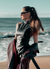 Beauty Fashion brunette model girl wearing stylish coat and sunglasses, posing on seaside. Sexy glamour woman portrait with perfect makeup, trendy fashion wear. Beauty trends. Fashion blogger. 