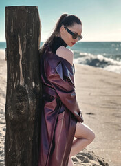 Beauty Fashion brunette model girl wearing stylish coat and sunglasses, posing on seaside. Sexy glamour woman portrait with perfect makeup, trendy fashion wear. Beauty trends. Fashion blogger - 772380836