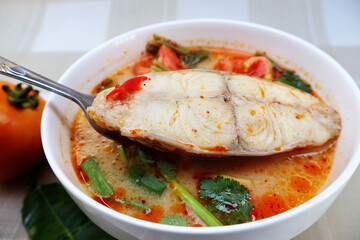 Use a fork to lift the fish pieces from the bowl of the spicy curry thickened with chilies and tomatoes and top with the greens.

