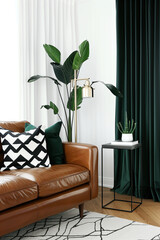 A living room with green velvet curtains, a leather sofa, and a black side table, plants on the coffee table, white walls, and a modern style of decoration.