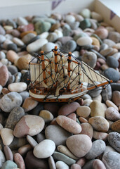 Vertical Concept Photo On Topic Of Sea Travel. Toy Sailing Vessel In Box Filled With Sea Rocks 
