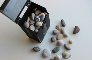 Black container mockup with colored pebbles inside and scattered pebbles near it on white surface

