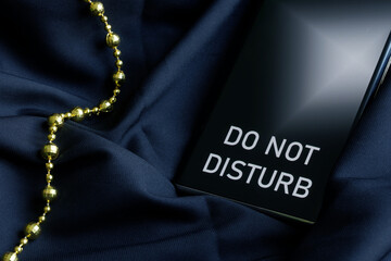 Smartphone cell phone with the inscription do not disturb next to decorative gold thread on a dark...