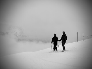 two skiers in dark clothing stand next to each other on the piste
