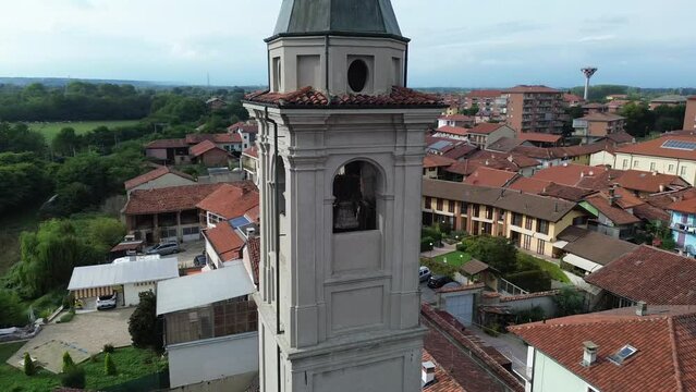 Drone footage of a bell tower of a church with European style houses on a sunny day with blue sky