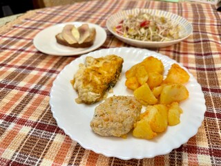 Three white plates on table. Salad of fresh vegetables and microgreens of sprouted mung beans. Fried potatoes with fish and meat patties. Herring sandwich with butter on colored background. Close-up