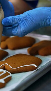 Decorating freshly-baked cookies with white cream. Confectioner squeezes icing from a pastry bag on the gingerbread cake. Close up. Vertical video