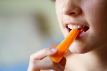 Anonymous young girl eating fresh organic carrot slice