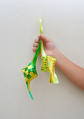 A child Hand holding traditional ketupat, made from yellow and green ribbon